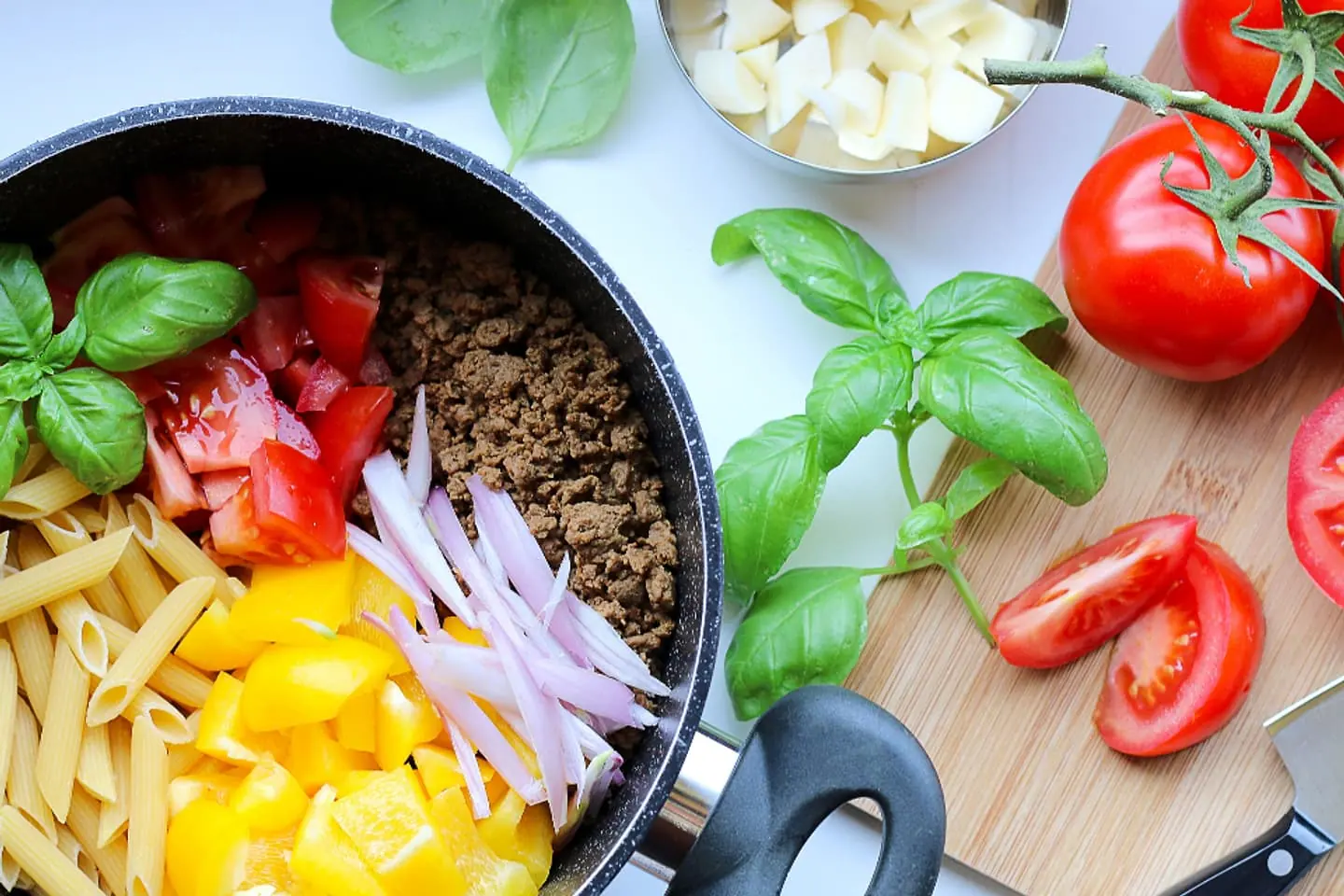 Pfanne mit Hackfleisch, Mais, Paprika und Käse, daneben Tomaten und Basilikum